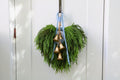 Cascading faux Norfolk pine wreath with dusty blue velvet ribbon and five gold-tone bells on rustic cord.