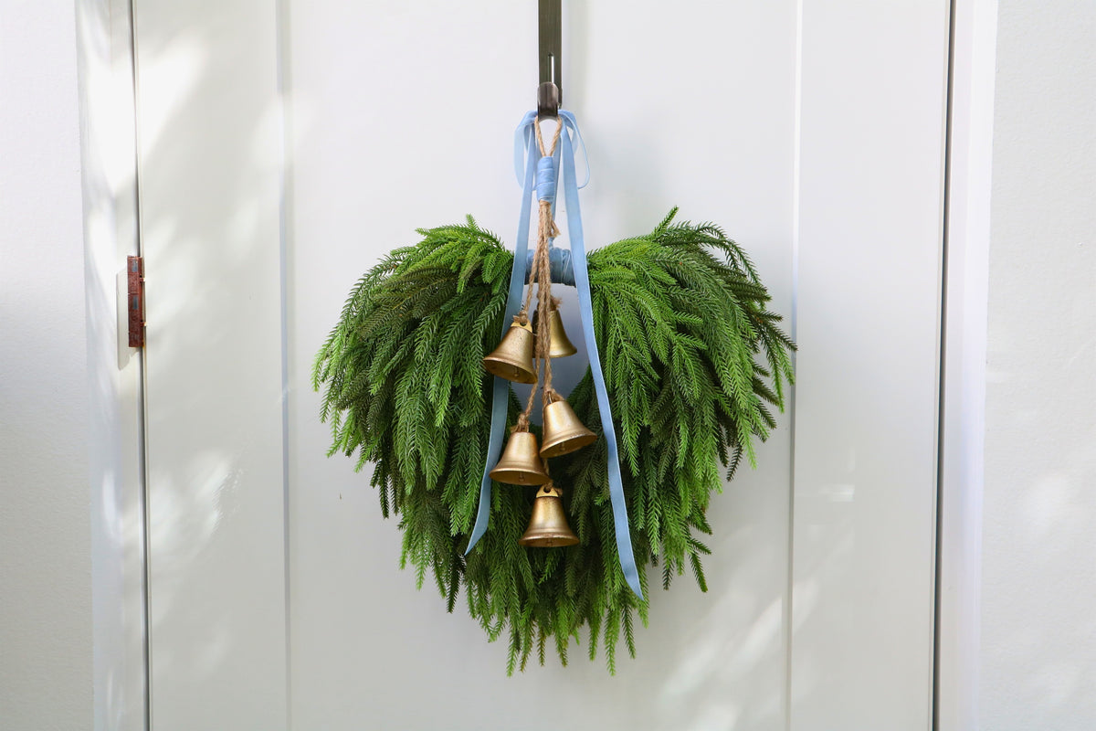 Cascading faux Norfolk pine wreath with dusty blue velvet ribbon and five gold-tone bells on rustic cord.