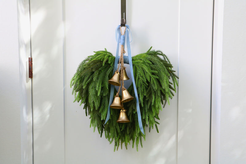 Cascading faux Norfolk pine wreath with dusty blue velvet ribbon and five gold-tone bells on rustic cord.