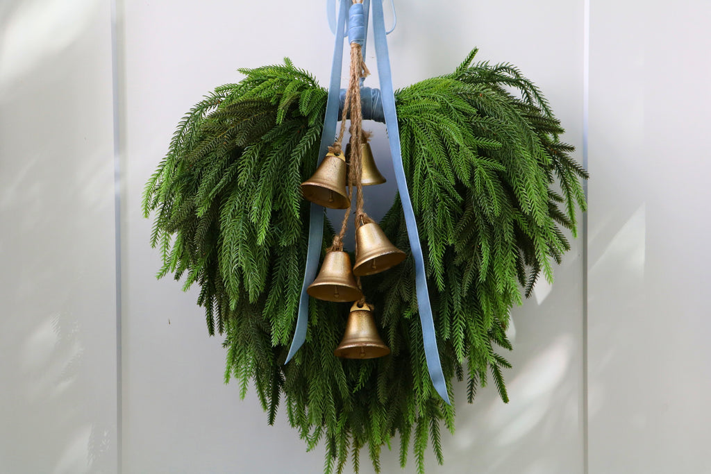 Cascading faux Norfolk pine wreath with dusty blue velvet ribbon and five gold-tone bells on rustic cord.