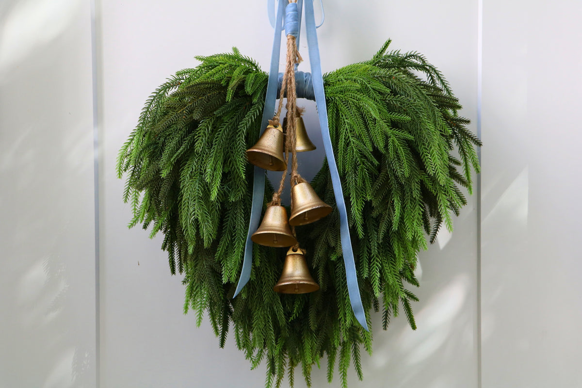 Cascading faux Norfolk pine wreath with dusty blue velvet ribbon and five gold-tone bells on rustic cord.
