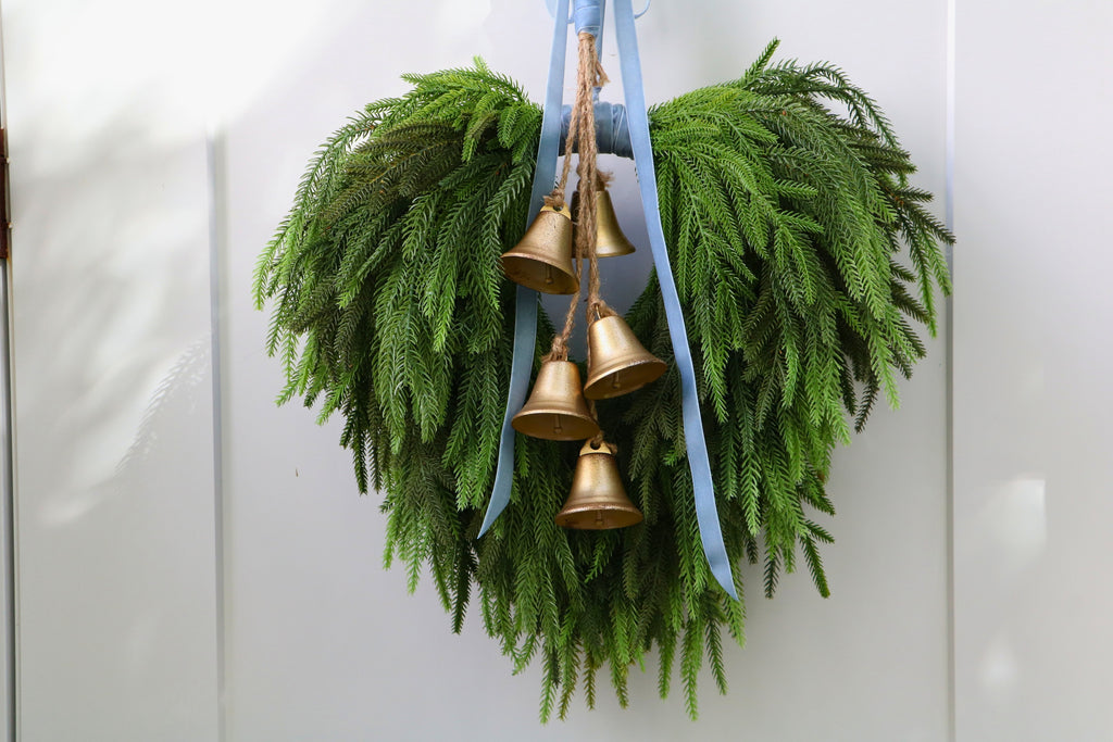 Cascading faux Norfolk pine wreath with dusty blue velvet ribbon and five gold-tone bells on rustic cord.