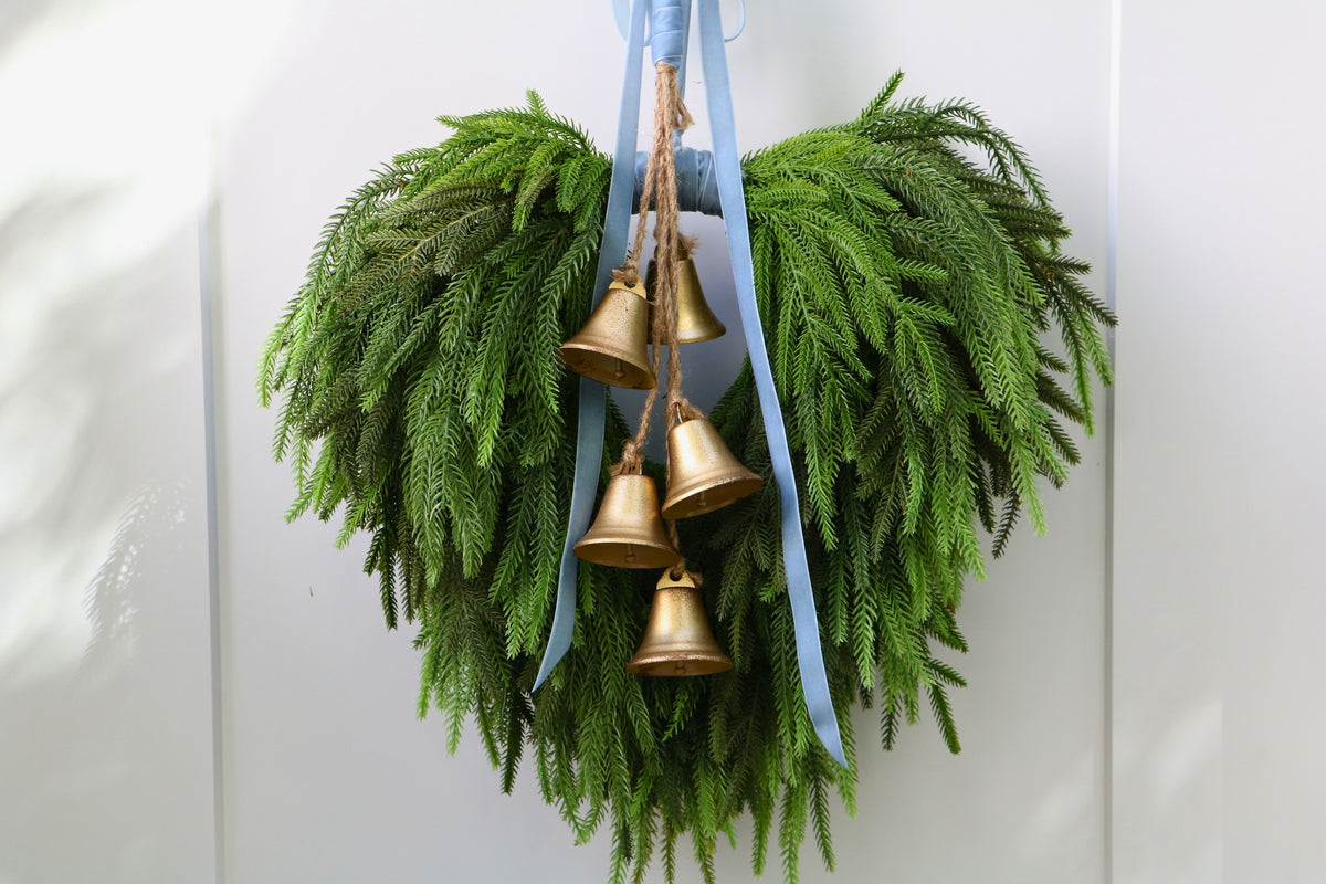 Cascading faux Norfolk pine wreath with dusty blue velvet ribbon and five gold-tone bells on rustic cord.