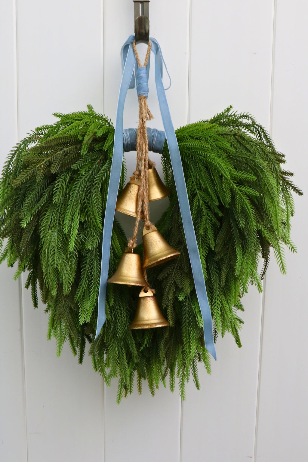Cascading faux Norfolk pine wreath with dusty blue velvet ribbon and five gold-tone bells on rustic cord.
