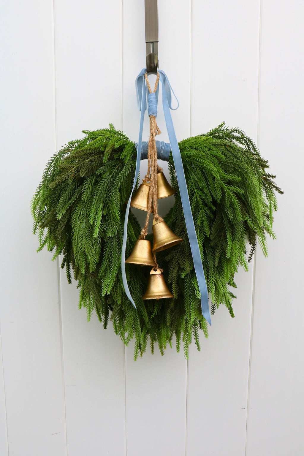 Cascading faux Norfolk pine wreath with dusty blue velvet ribbon and five gold-tone bells on rustic cord.