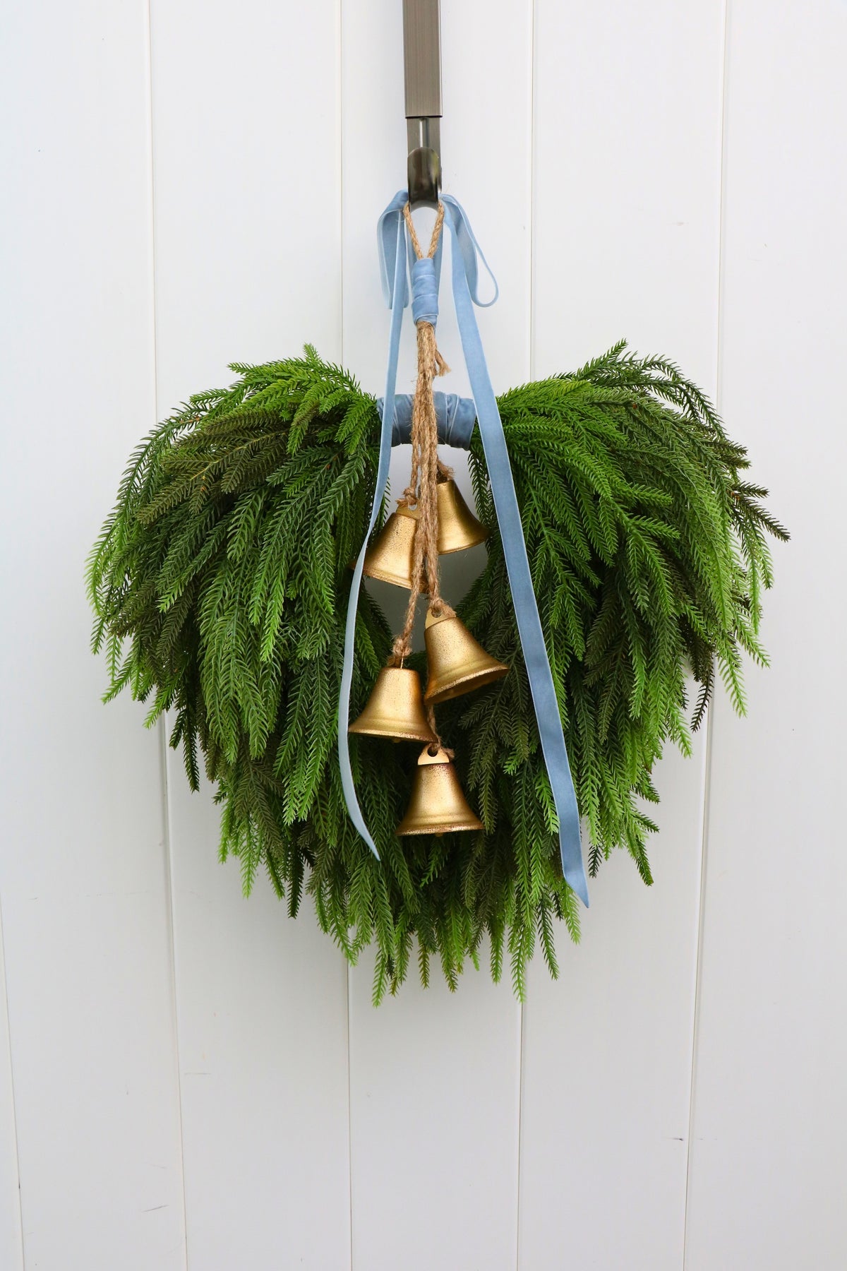 Cascading faux Norfolk pine wreath with dusty blue velvet ribbon and five gold-tone bells on rustic cord.
