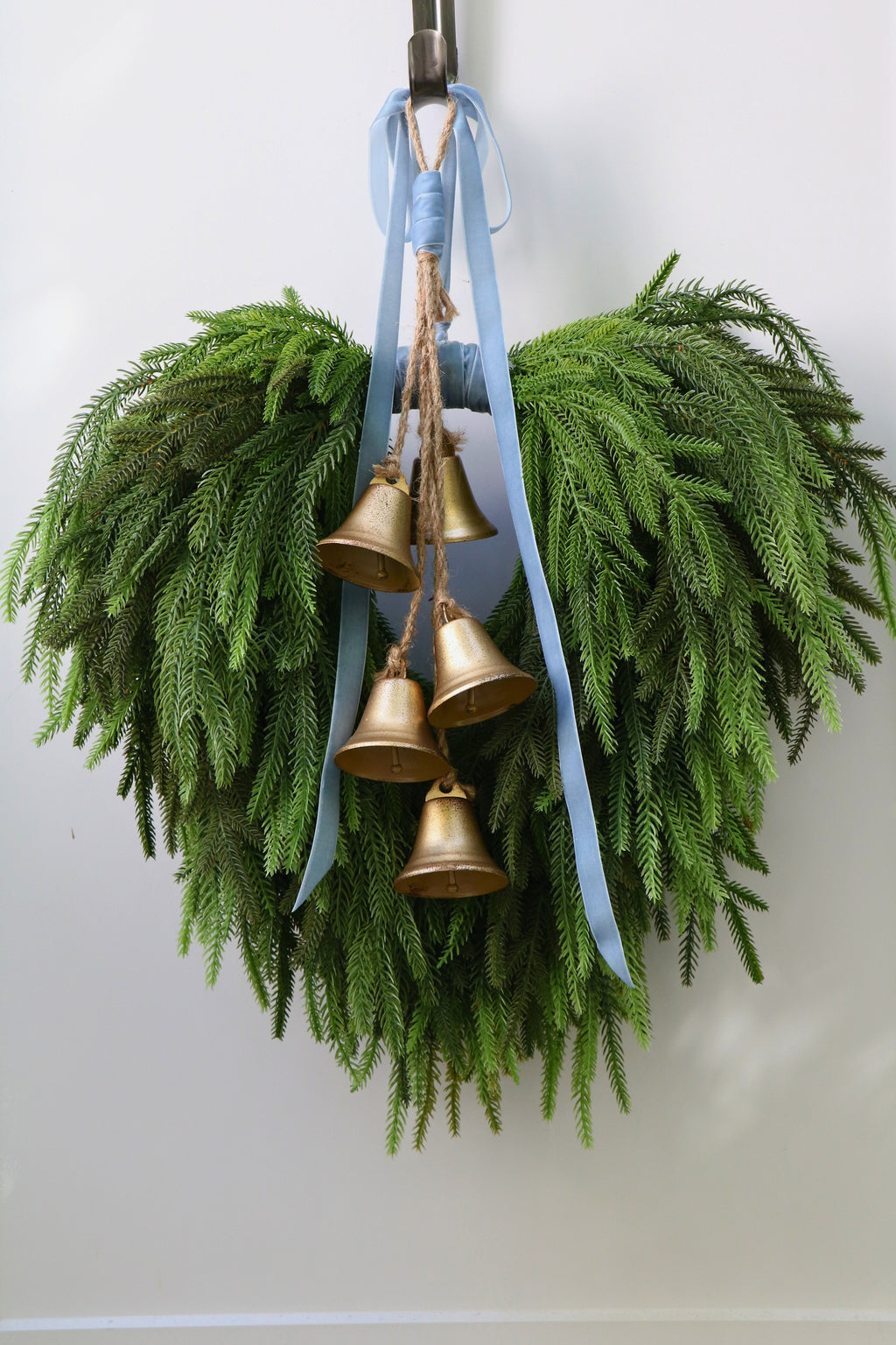 Cascading faux Norfolk pine wreath with dusty blue velvet ribbon and five gold-tone bells on rustic cord.