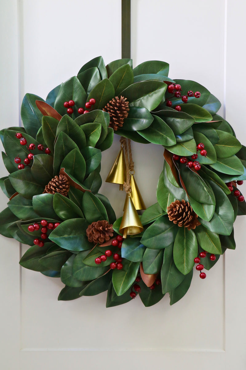 Magnolia leaf wreath with red berry clusters, four pinecones and three hanging gold-tone bells.