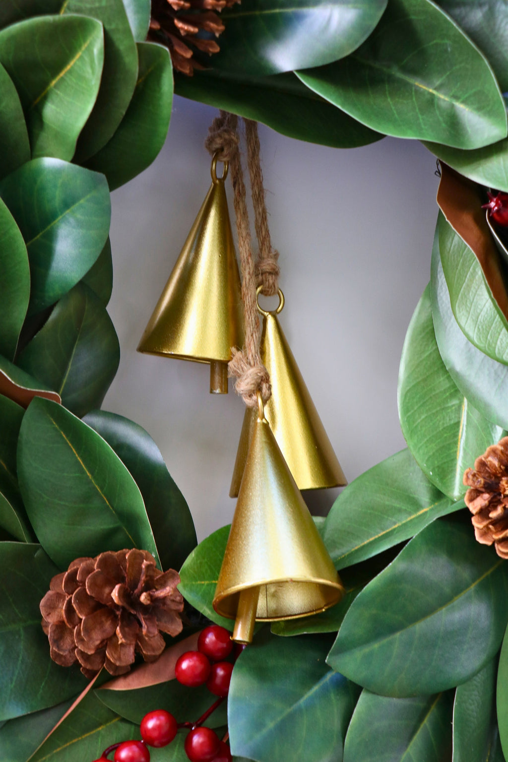 Magnolia leaf wreath with red berry clusters, four pinecones and three hanging gold-tone bells.