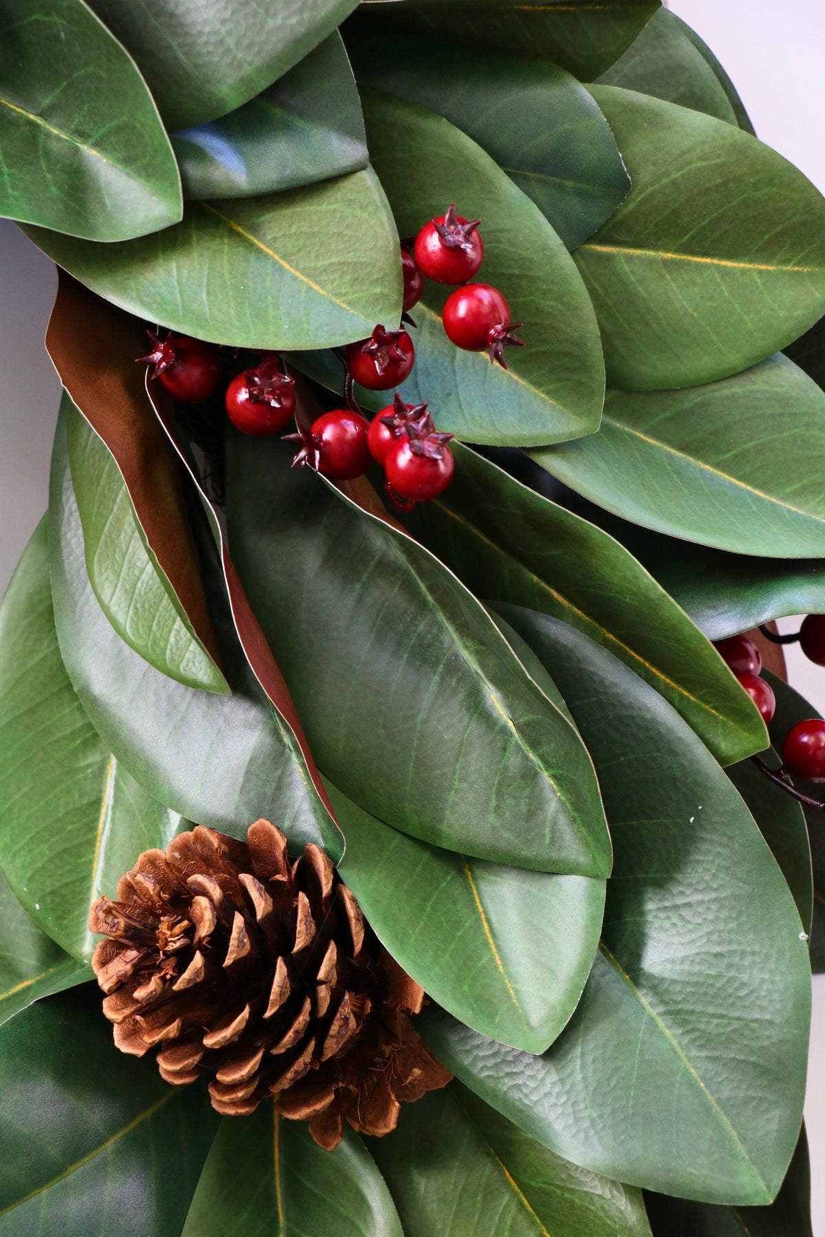 Magnolia leaf wreath with red berry clusters, four pinecones and three hanging gold-tone bells.