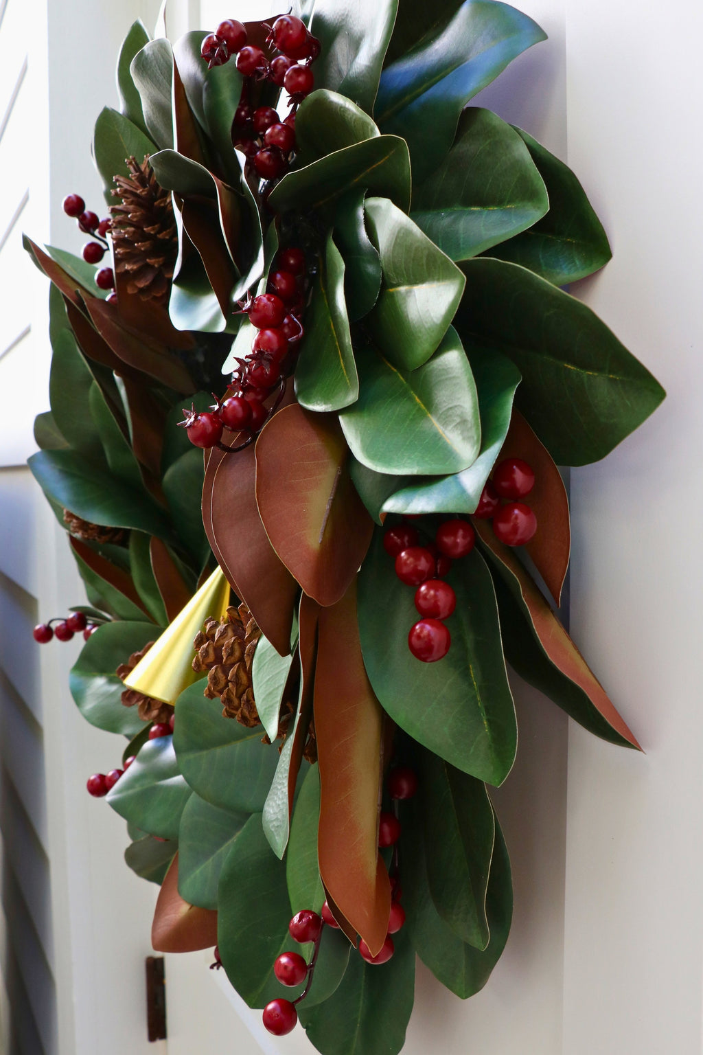 Magnolia leaf wreath with red berry clusters, four pinecones and three hanging gold-tone bells.