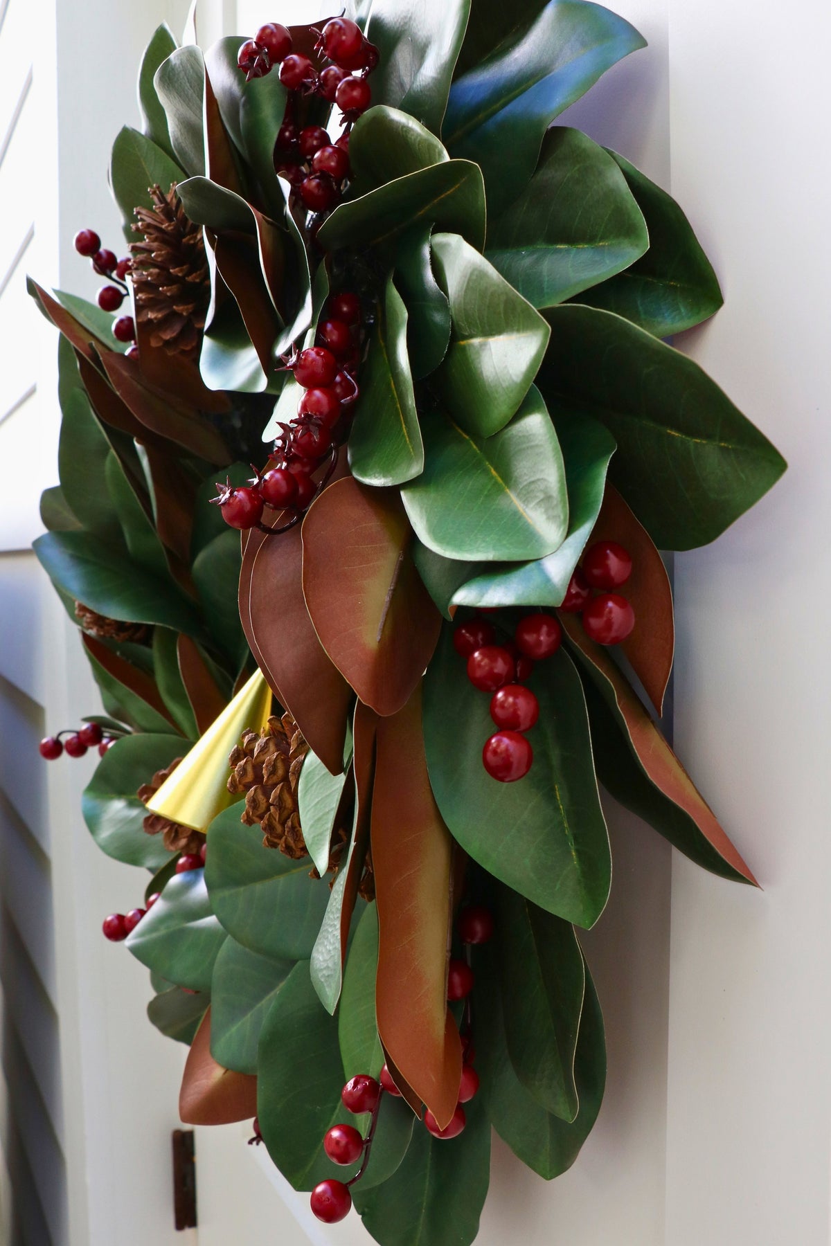 Magnolia leaf wreath with red berry clusters, four pinecones and three hanging gold-tone bells.