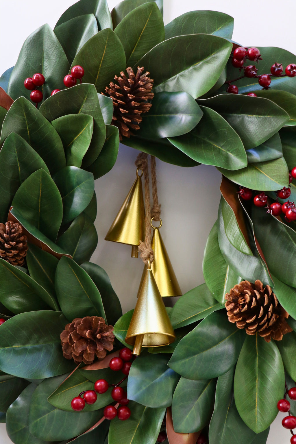 Magnolia leaf wreath with red berry clusters, four pinecones and three hanging gold-tone bells.