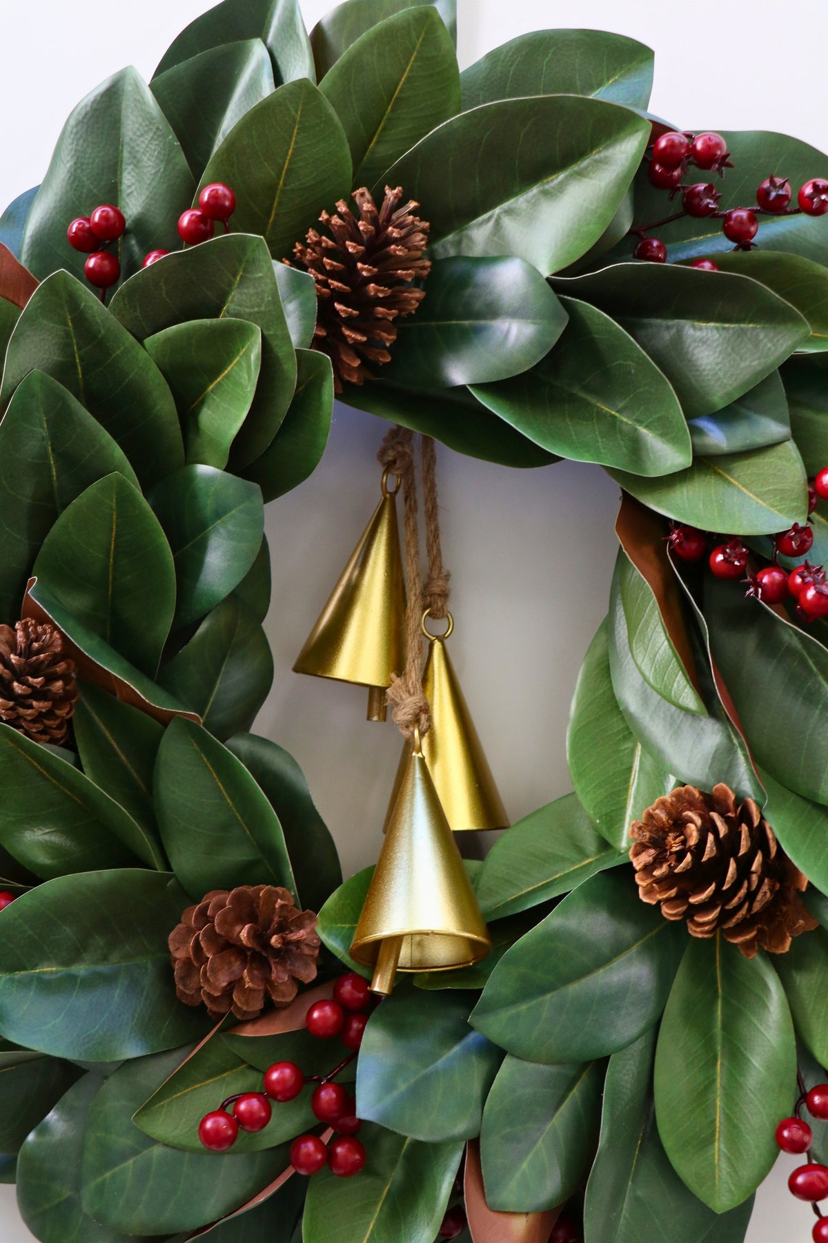 Magnolia leaf wreath with red berry clusters, four pinecones and three hanging gold-tone bells.
