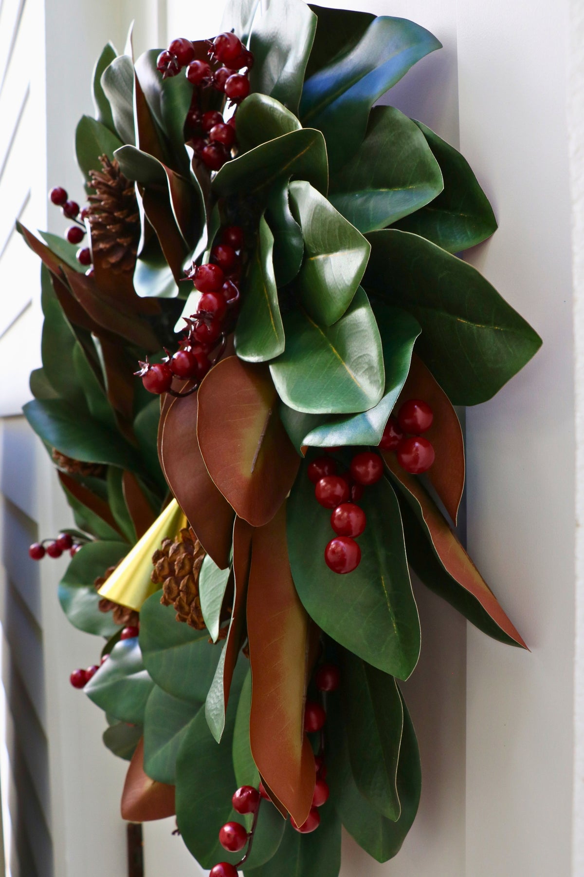 Magnolia leaf wreath with red berry clusters, four pinecones and three hanging gold-tone bells.