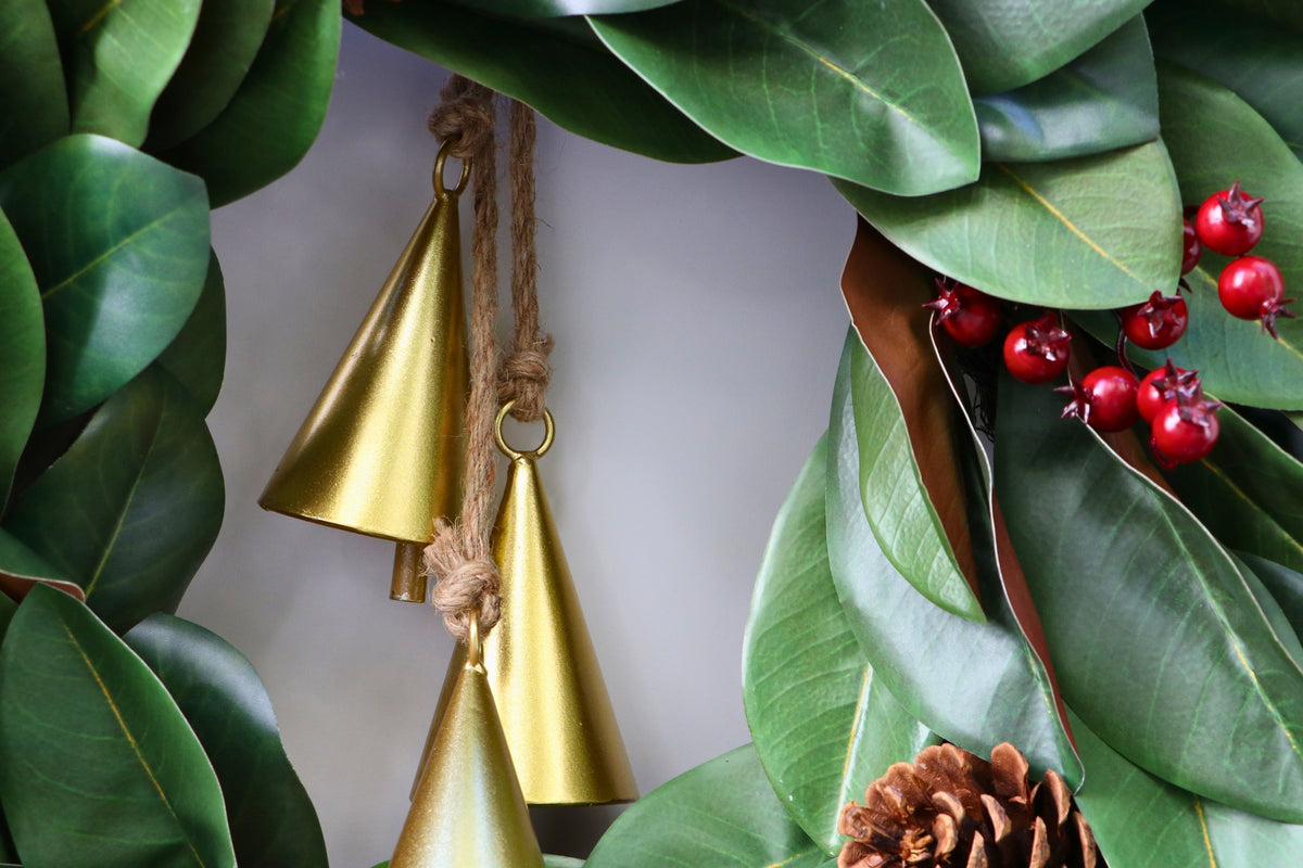 Magnolia leaf wreath with red berry clusters, four pinecones and three hanging gold-tone bells.