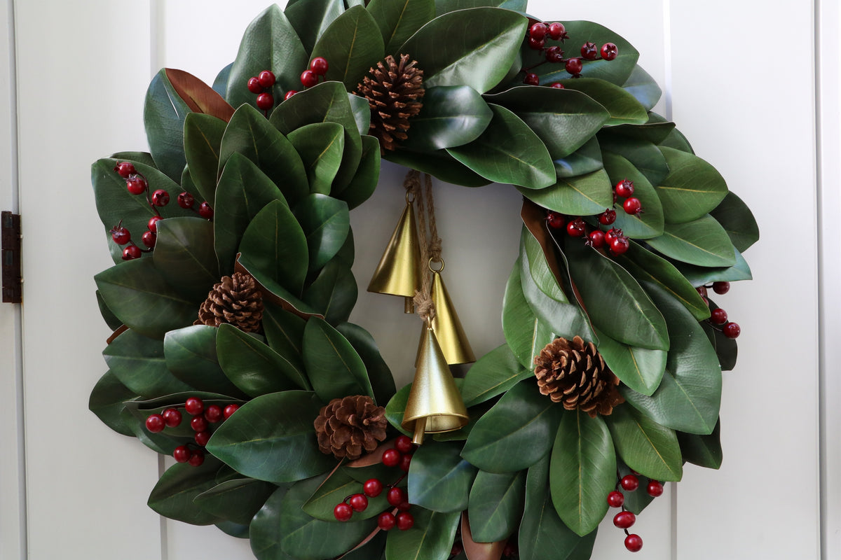 Magnolia leaf wreath with red berry clusters, four pinecones and three hanging gold-tone bells.