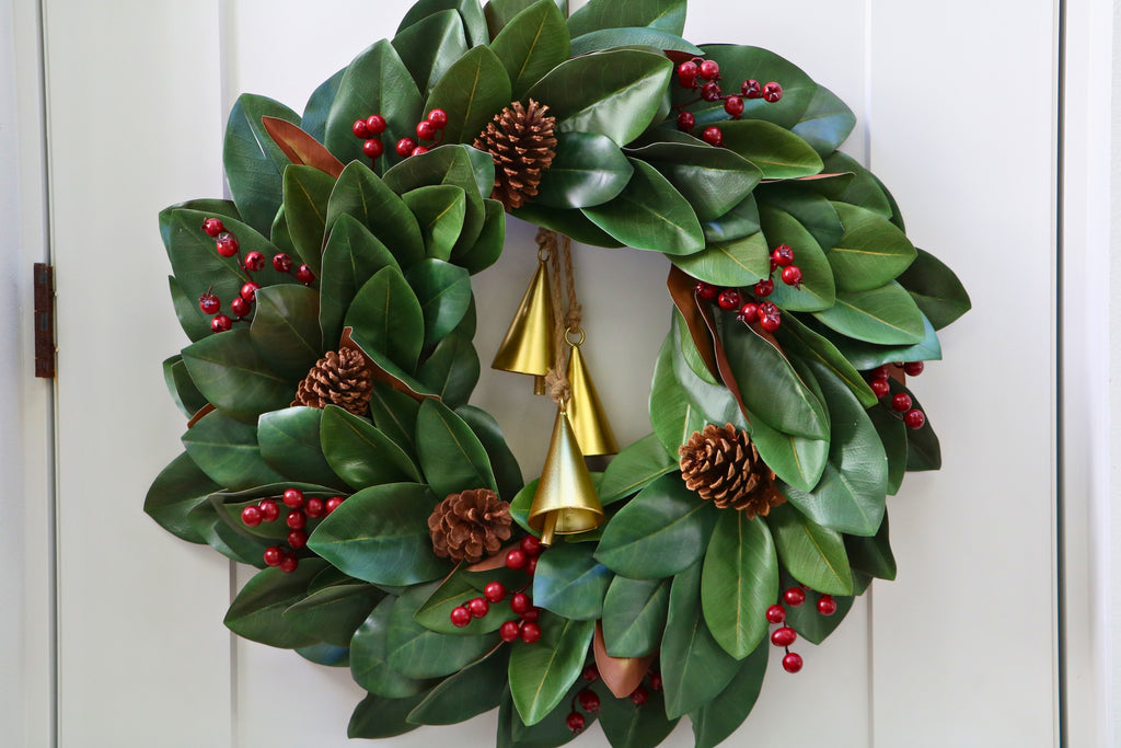 Magnolia leaf wreath with red berry clusters, four pinecones and three hanging gold-tone bells.