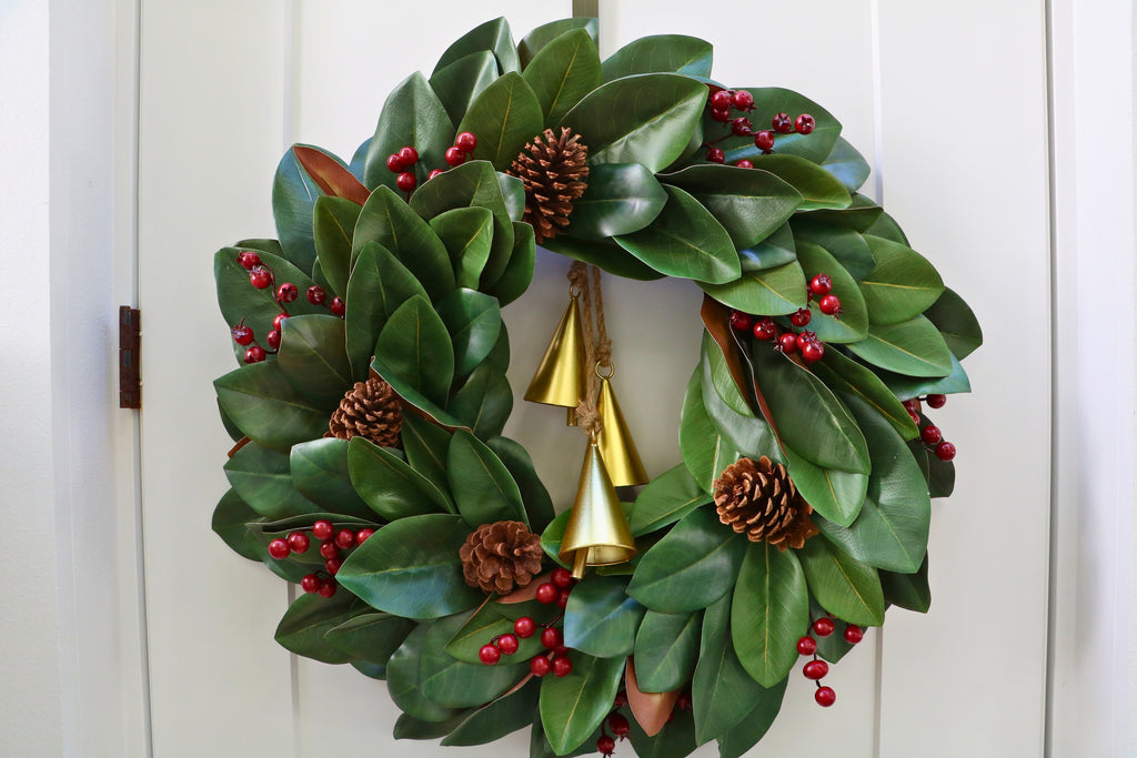 Magnolia leaf wreath with red berry clusters, four pinecones and three hanging gold-tone bells.