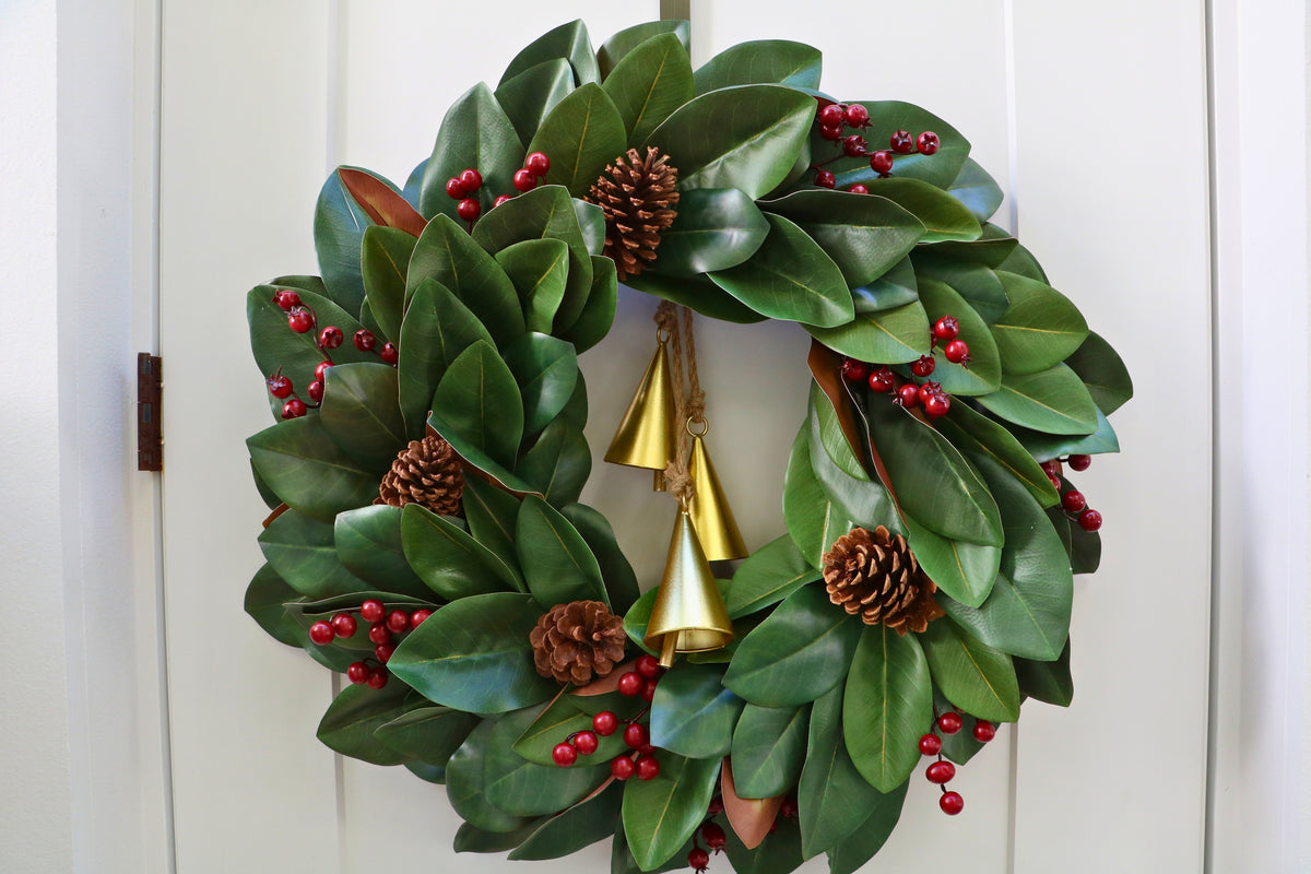 Magnolia leaf wreath with red berry clusters, four pinecones and three hanging gold-tone bells.