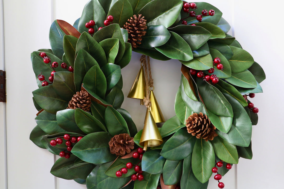 Magnolia leaf wreath with red berry clusters, four pinecones and three hanging gold-tone bells.