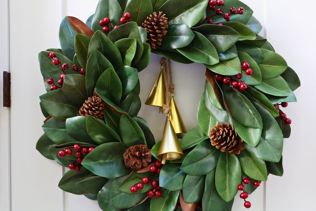 Magnolia leaf wreath with red berry clusters, four pinecones and three hanging gold-tone bells.