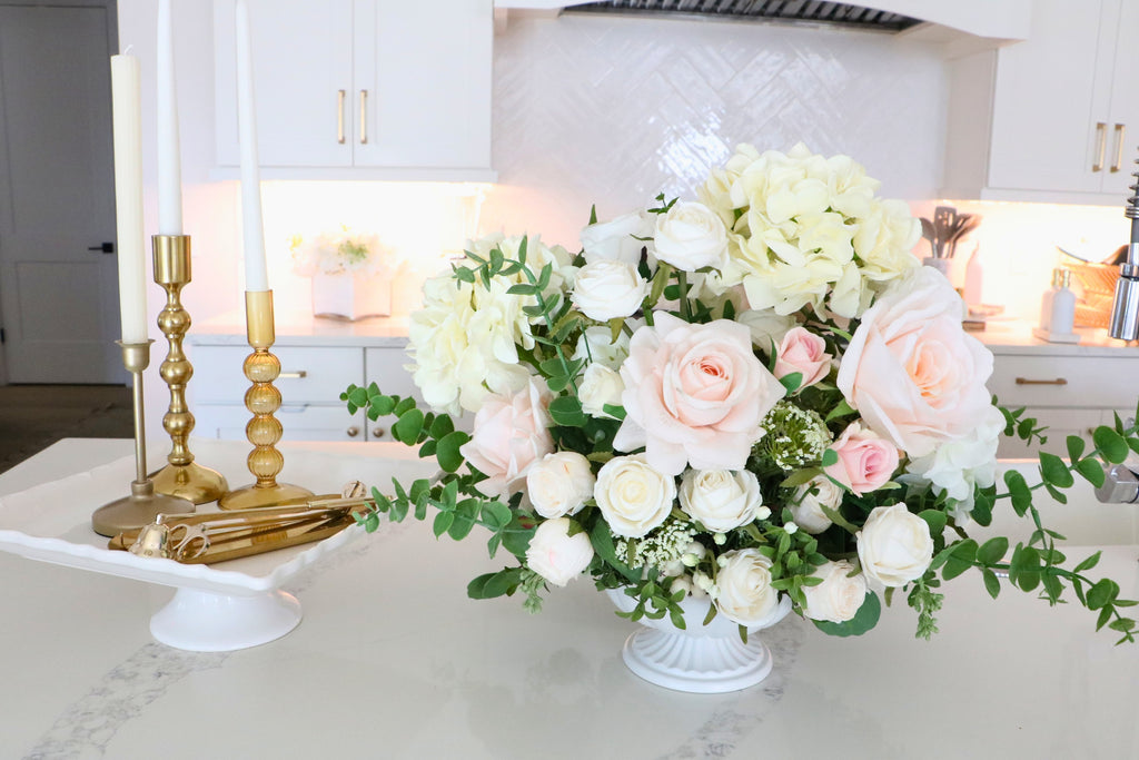 Ivory and blush rose and hydrangea arrangement with eucalyptus in a white pedestal-style compote vase.