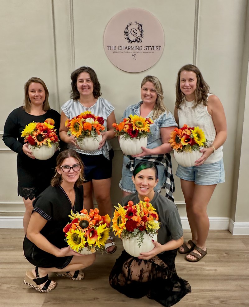 Six workshop guests holding their finished autumn floral arrangements in white pumpkins.