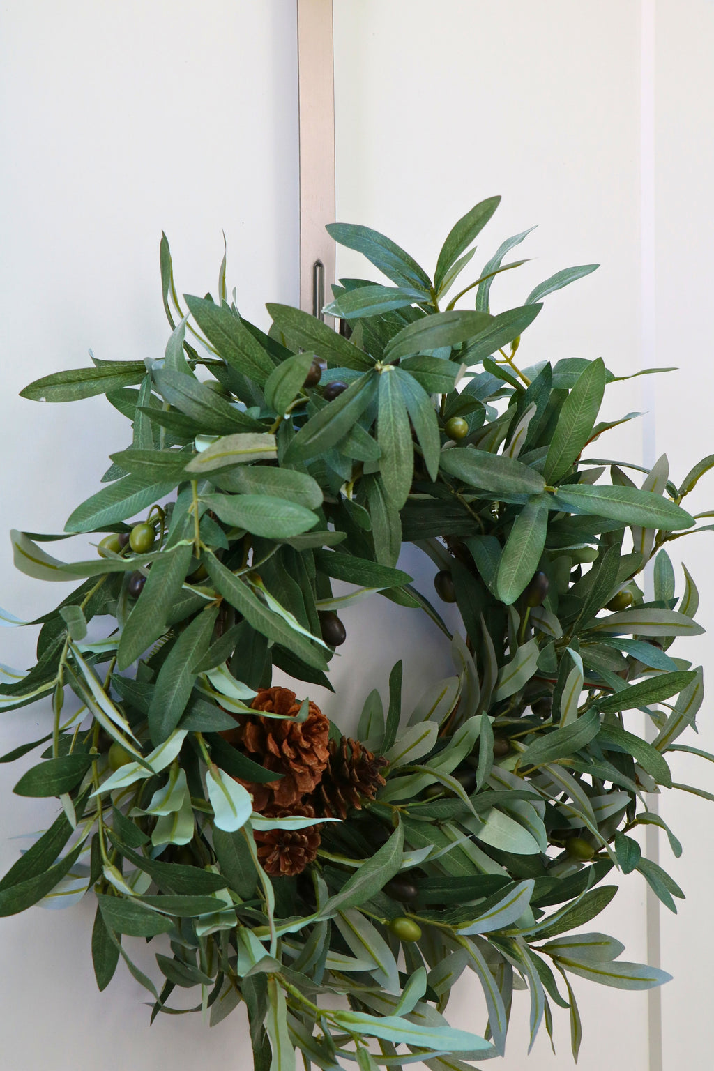 Faux olive wreath with green leaves, decorative olives and a cluster of brown pinecones.