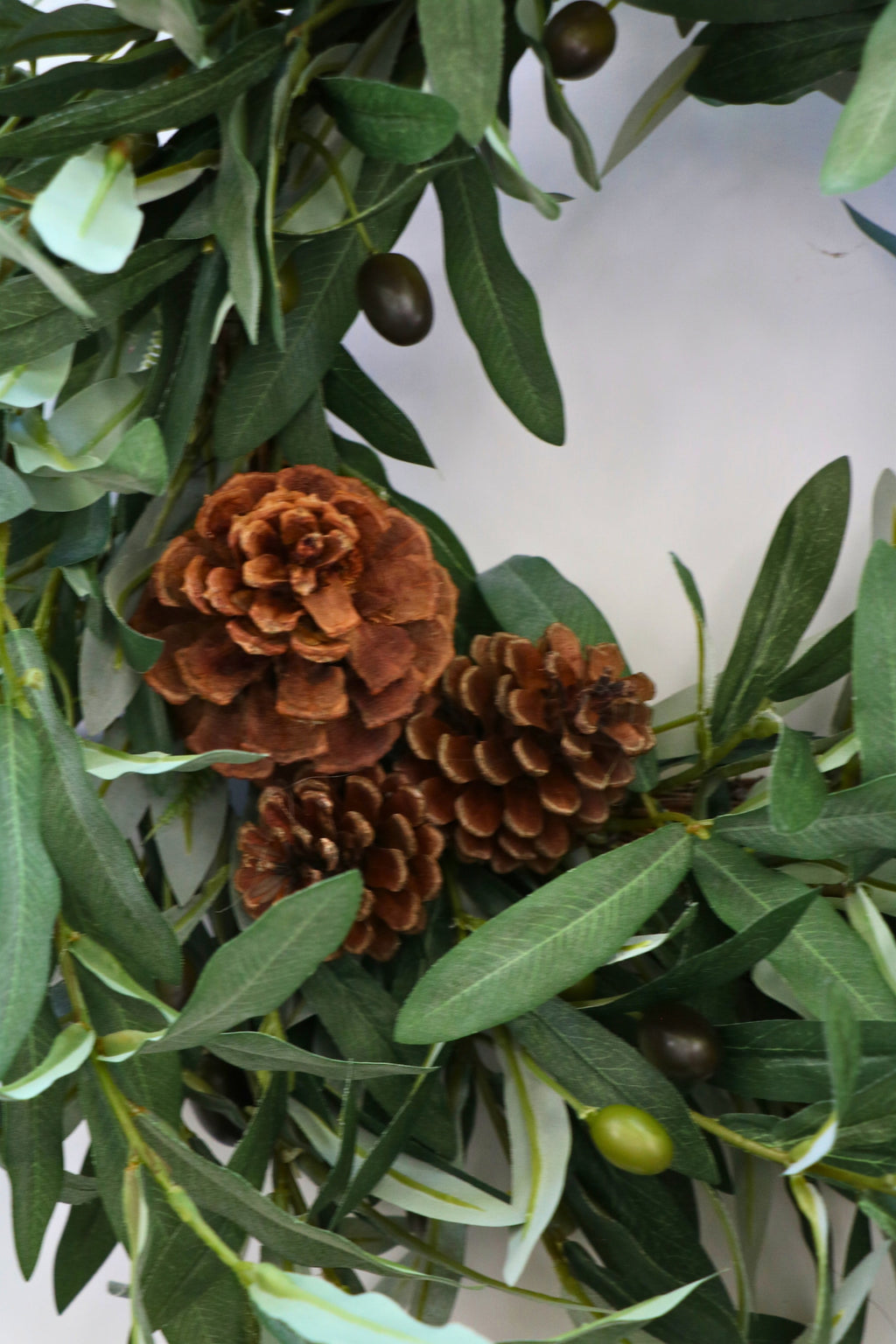 Faux olive wreath with green leaves, decorative olives and a cluster of brown pinecones.