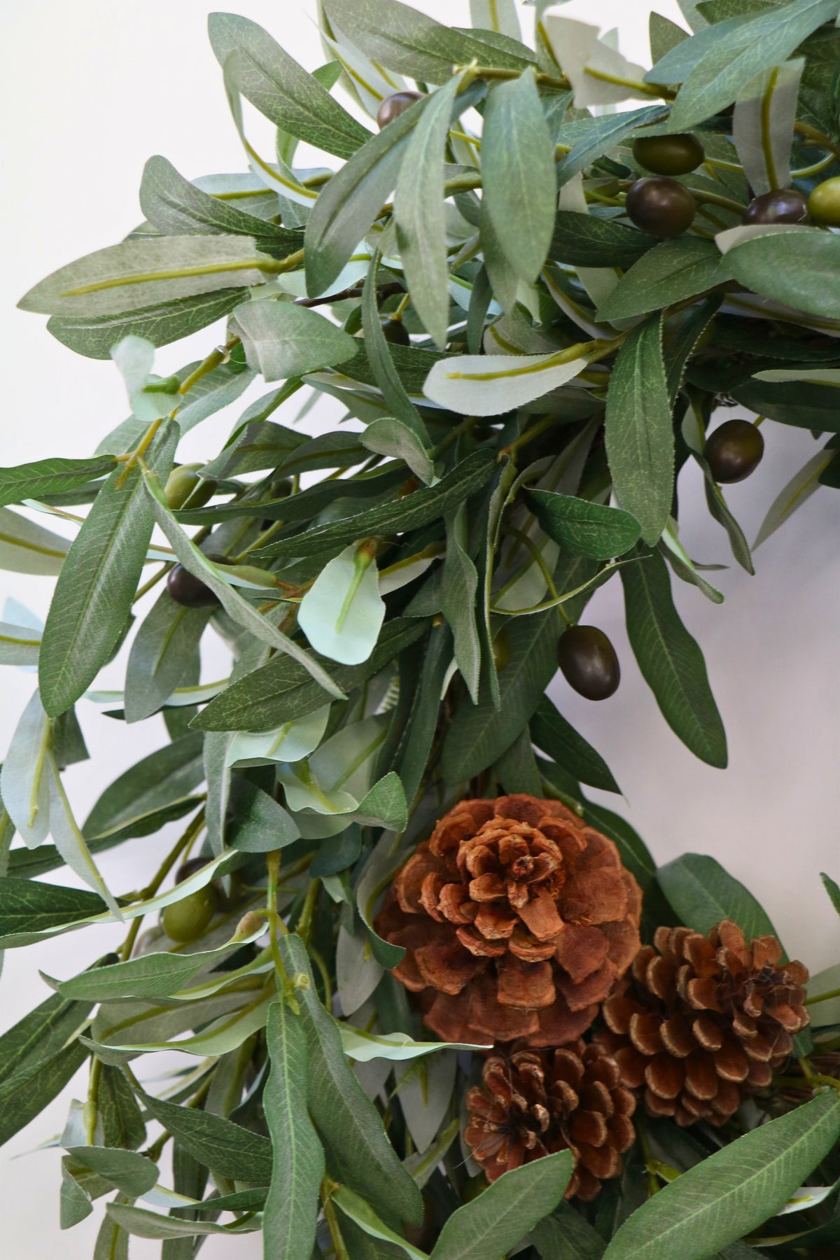 Faux olive wreath with green leaves, decorative olives and a cluster of brown pinecones.