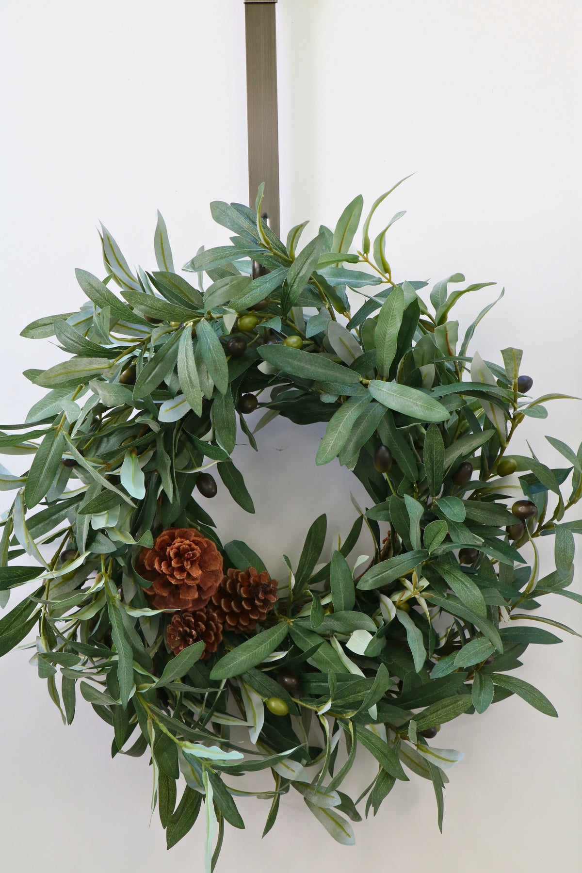Faux olive wreath with green leaves, decorative olives and a cluster of brown pinecones.