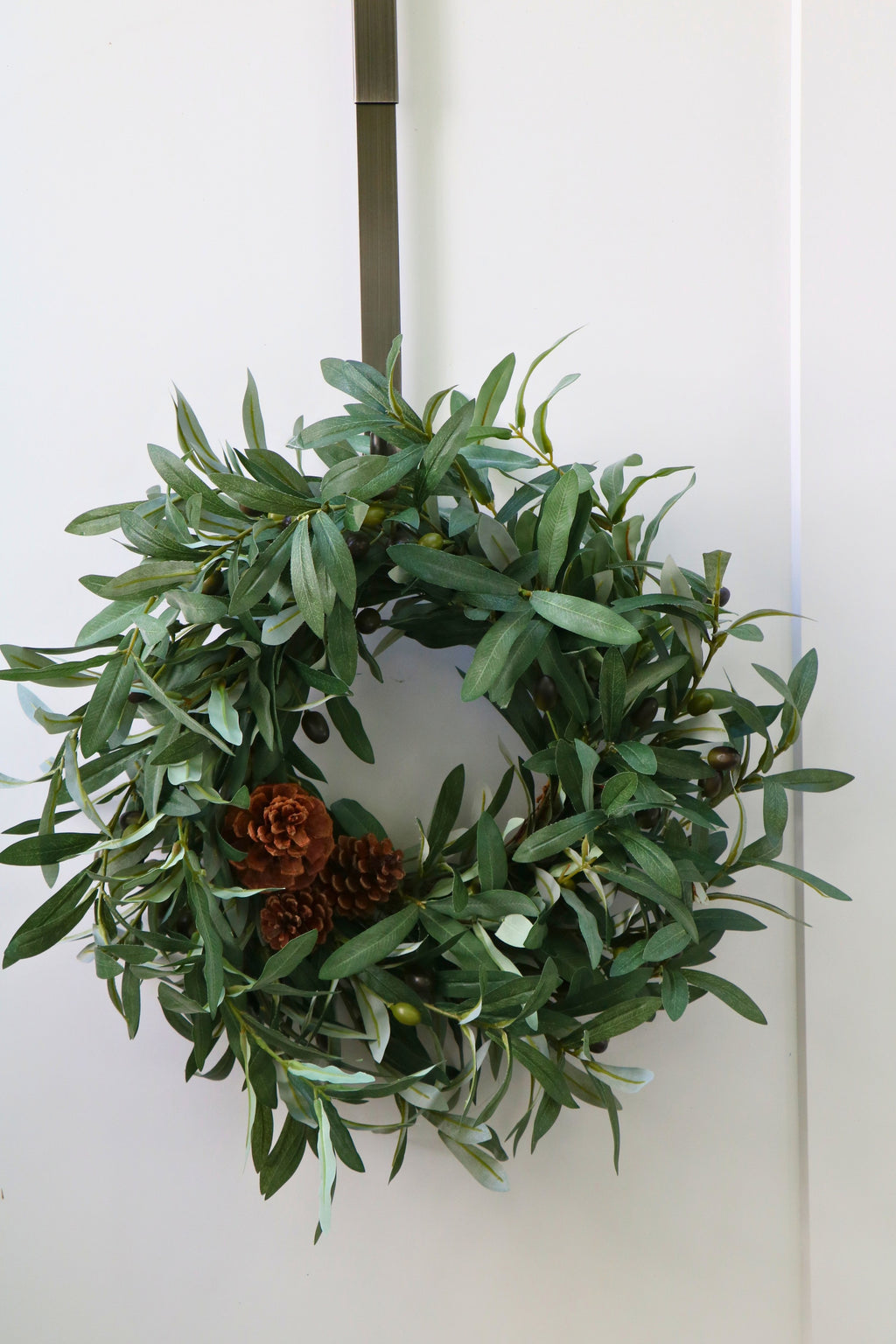 Faux olive wreath with green leaves, decorative olives and a cluster of brown pinecones.