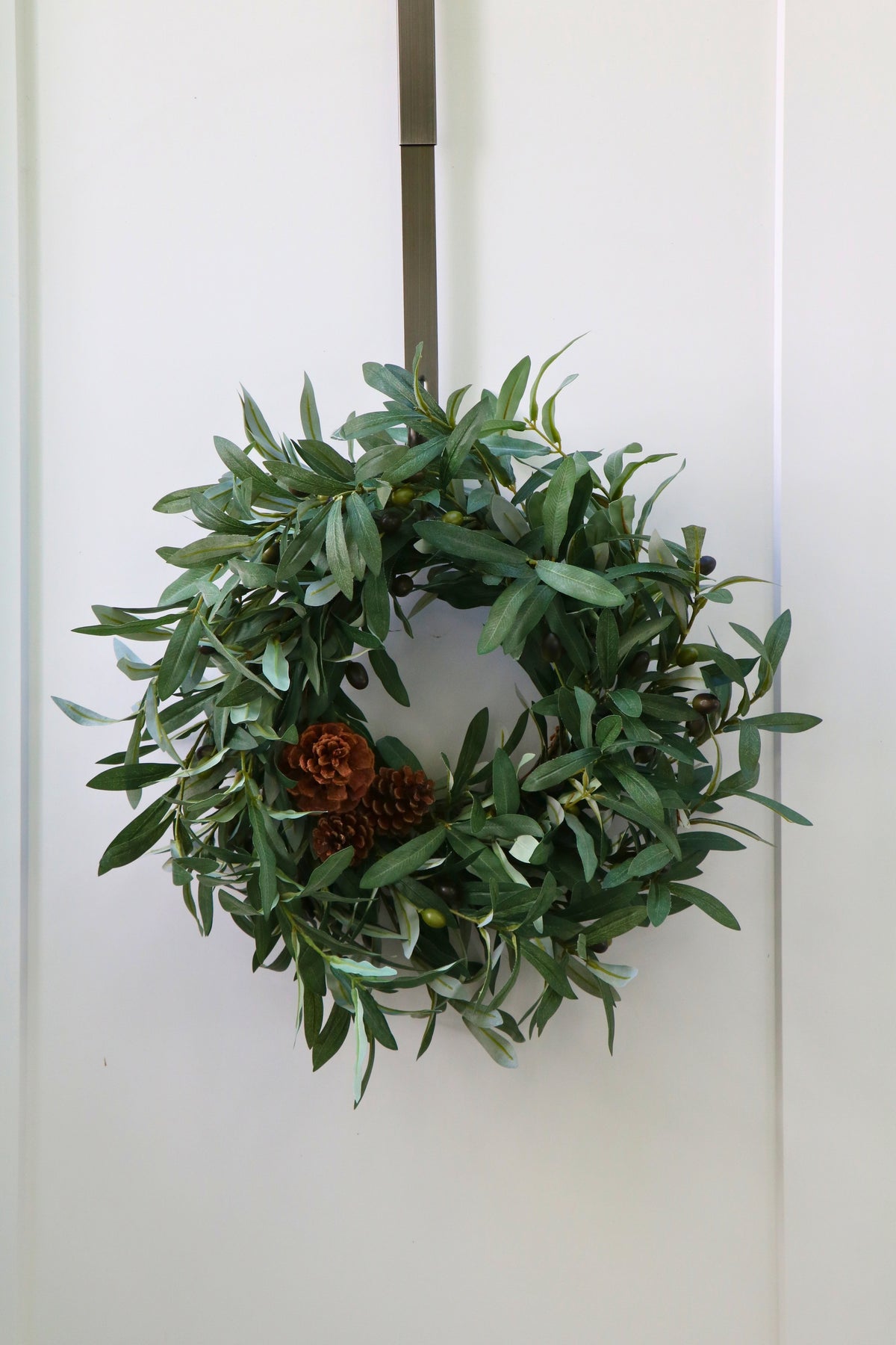 Faux olive wreath with green leaves, decorative olives and a cluster of brown pinecones.