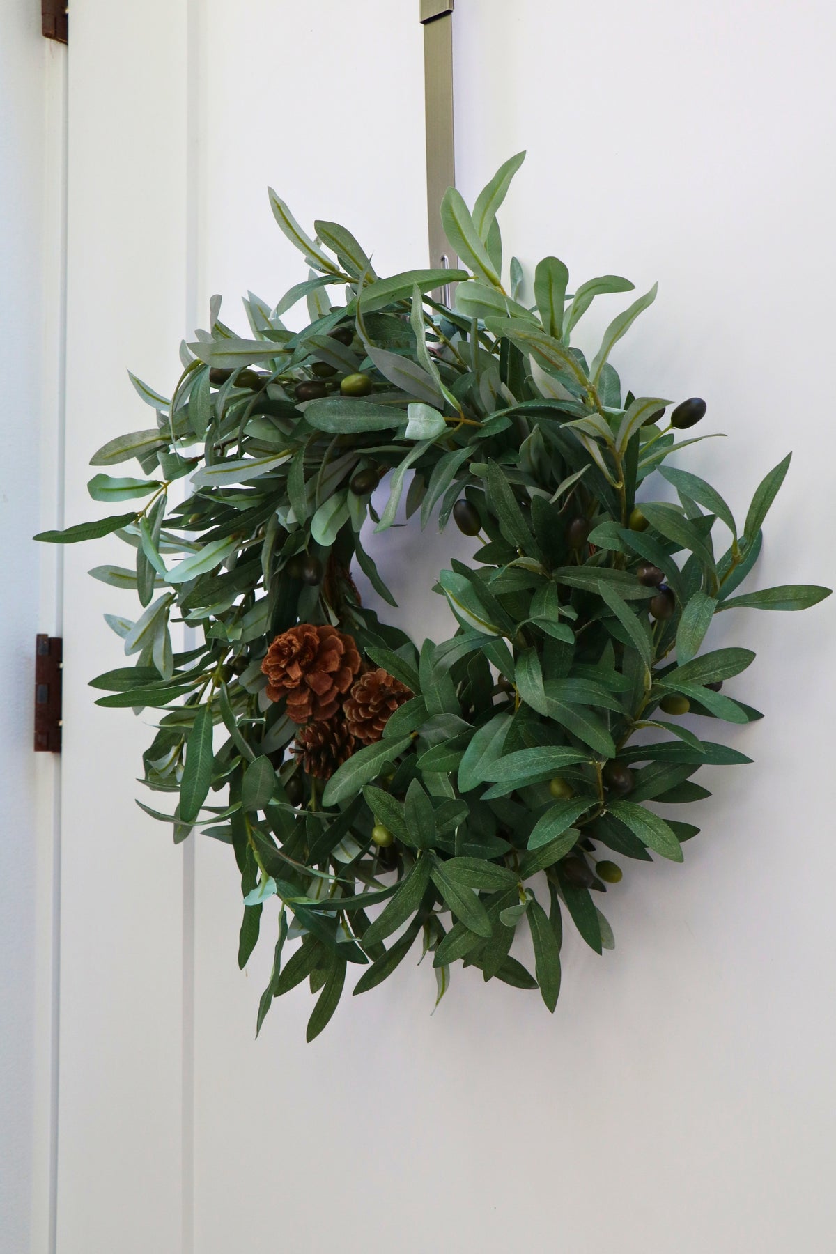 Faux olive wreath with green leaves, decorative olives and a cluster of brown pinecones.