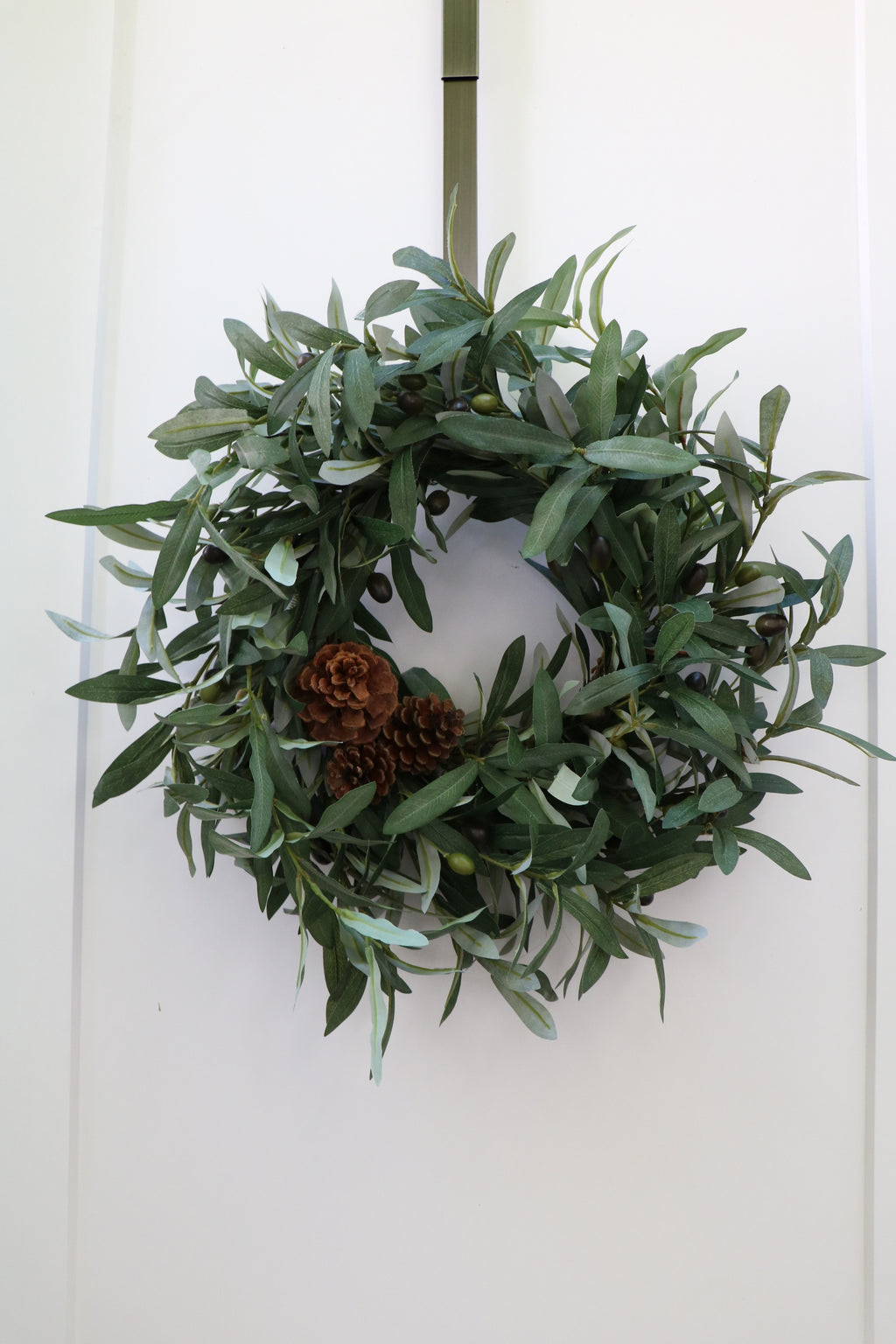 Faux olive wreath with green leaves, decorative olives and a cluster of brown pinecones.