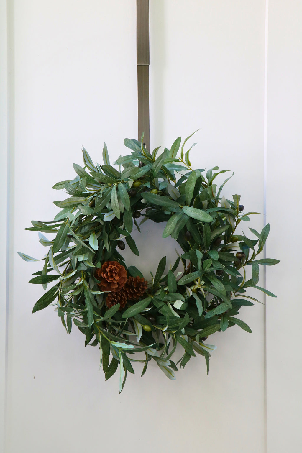 Faux olive wreath with green leaves, decorative olives and a cluster of brown pinecones.
