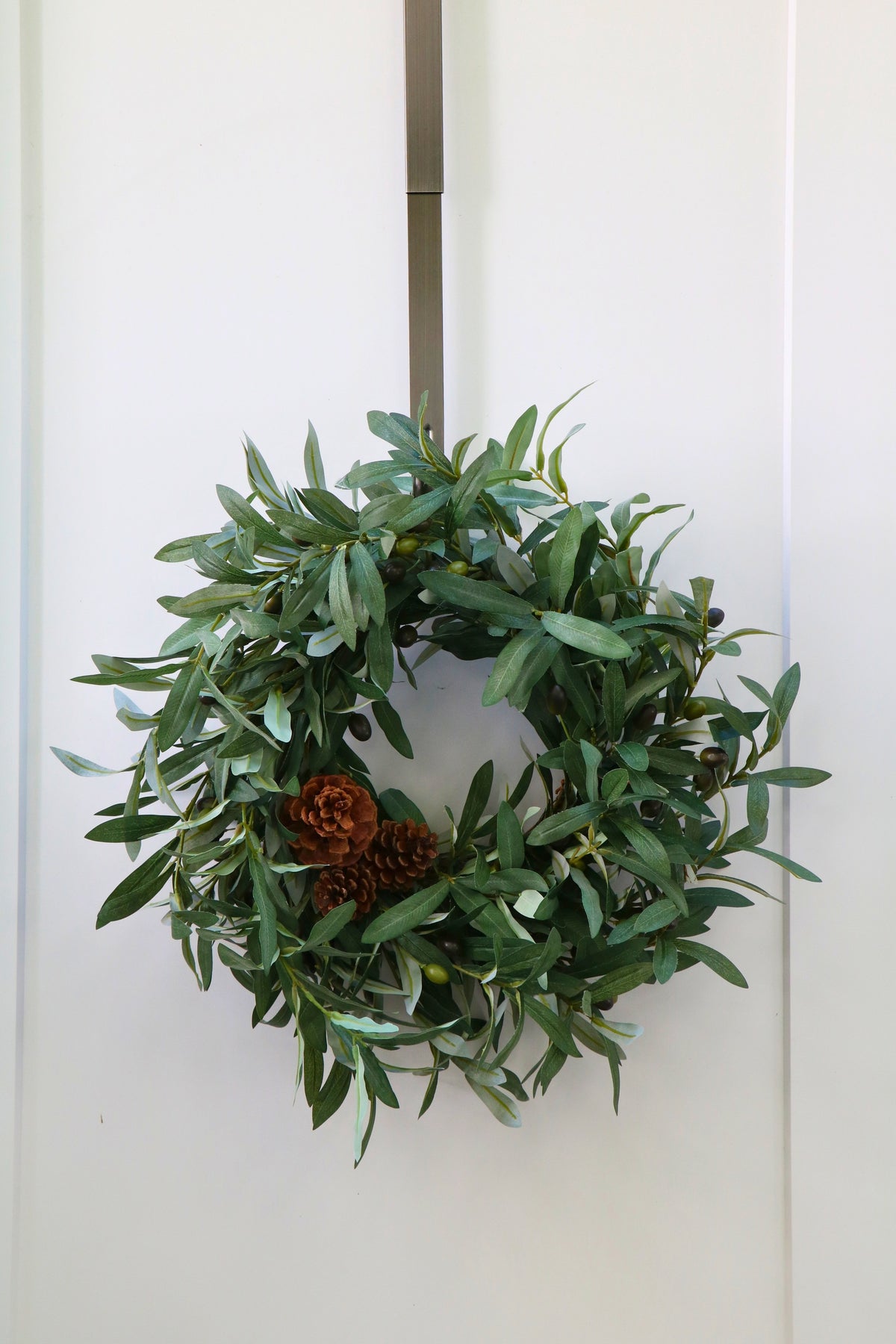 Faux olive wreath with green leaves, decorative olives and a cluster of brown pinecones.