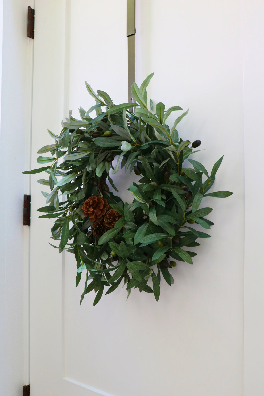 Faux olive wreath with green leaves, decorative olives and a cluster of brown pinecones.