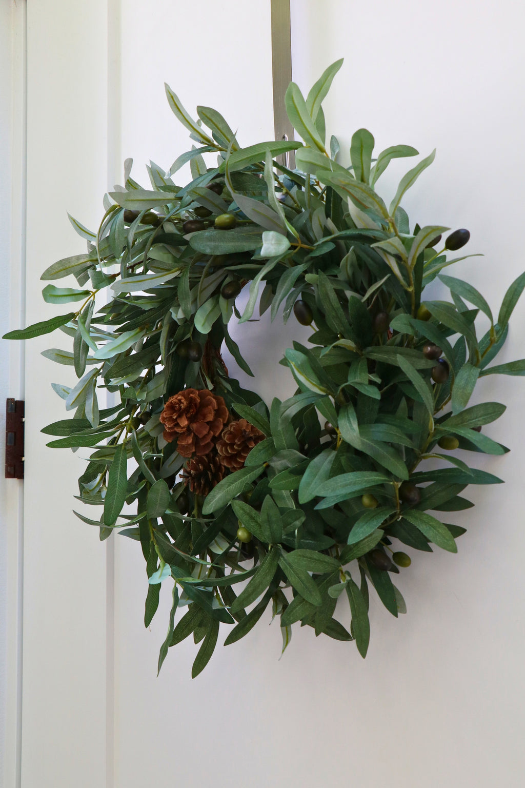 Faux olive wreath with green leaves, decorative olives and a cluster of brown pinecones.