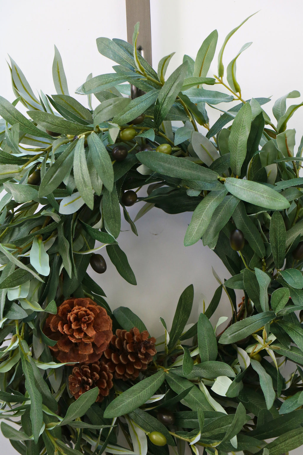 Faux olive wreath with green leaves, decorative olives and a cluster of brown pinecones.