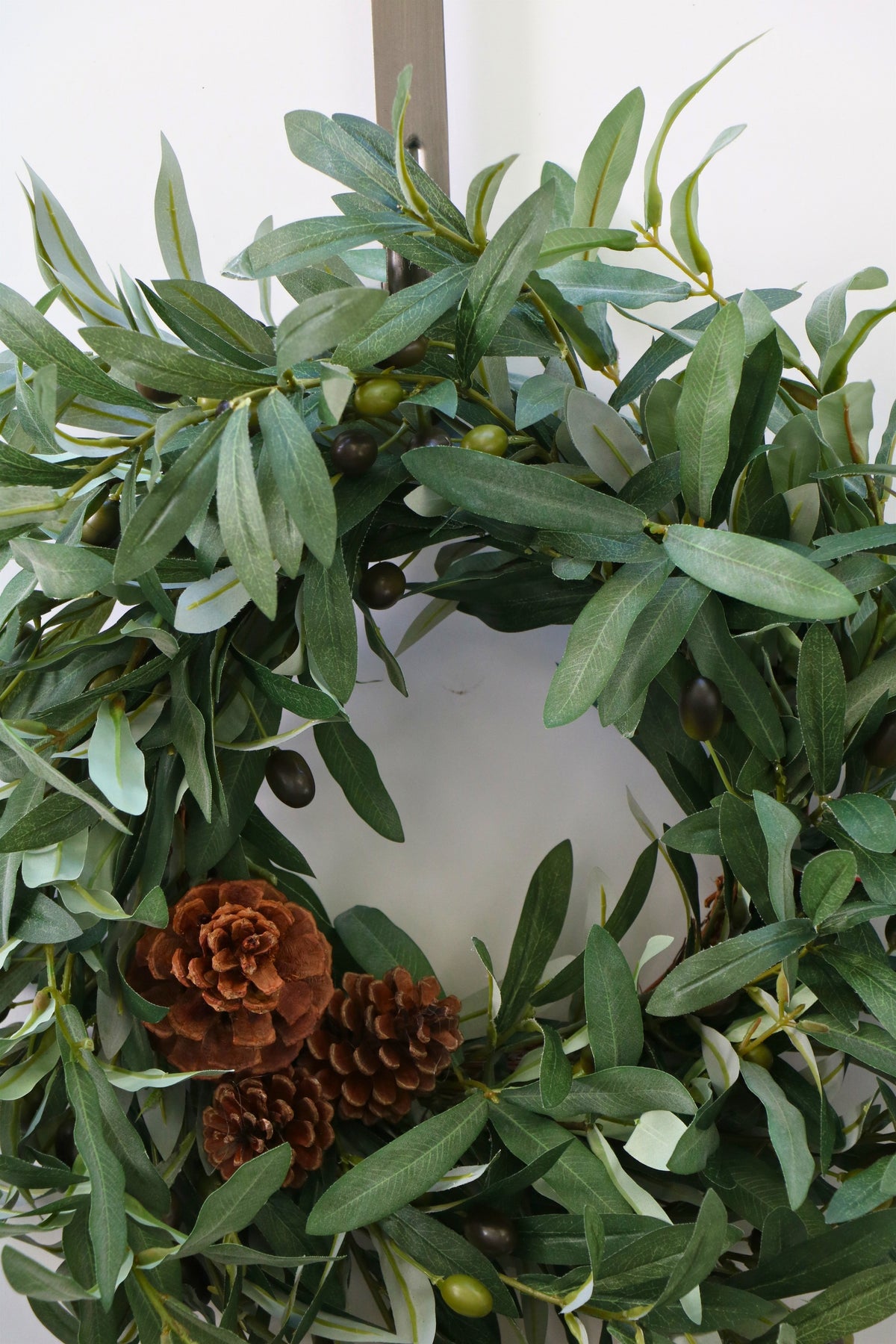 Faux olive wreath with green leaves, decorative olives and a cluster of brown pinecones.