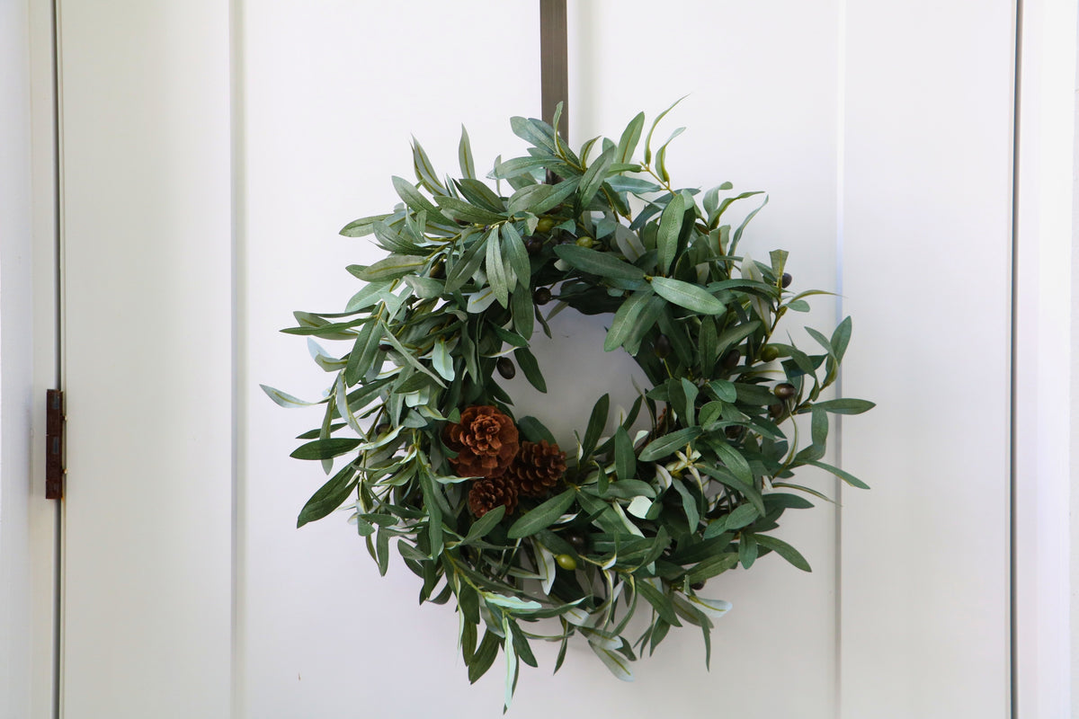 Faux olive wreath with green leaves, decorative olives and a cluster of brown pinecones.