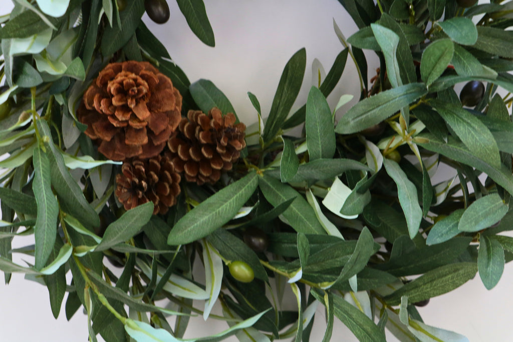 Faux olive wreath with green leaves, decorative olives and a cluster of brown pinecones.