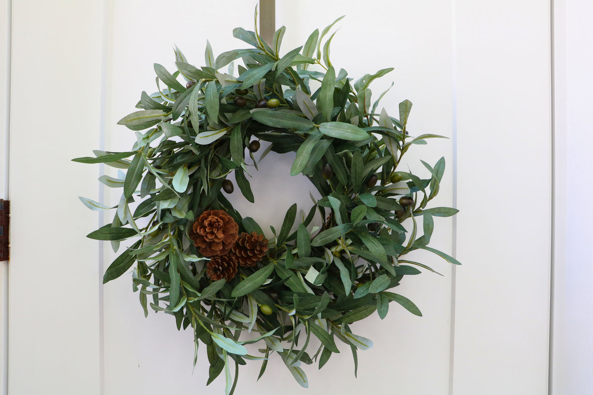 Faux olive wreath with green leaves, decorative olives and a cluster of brown pinecones.