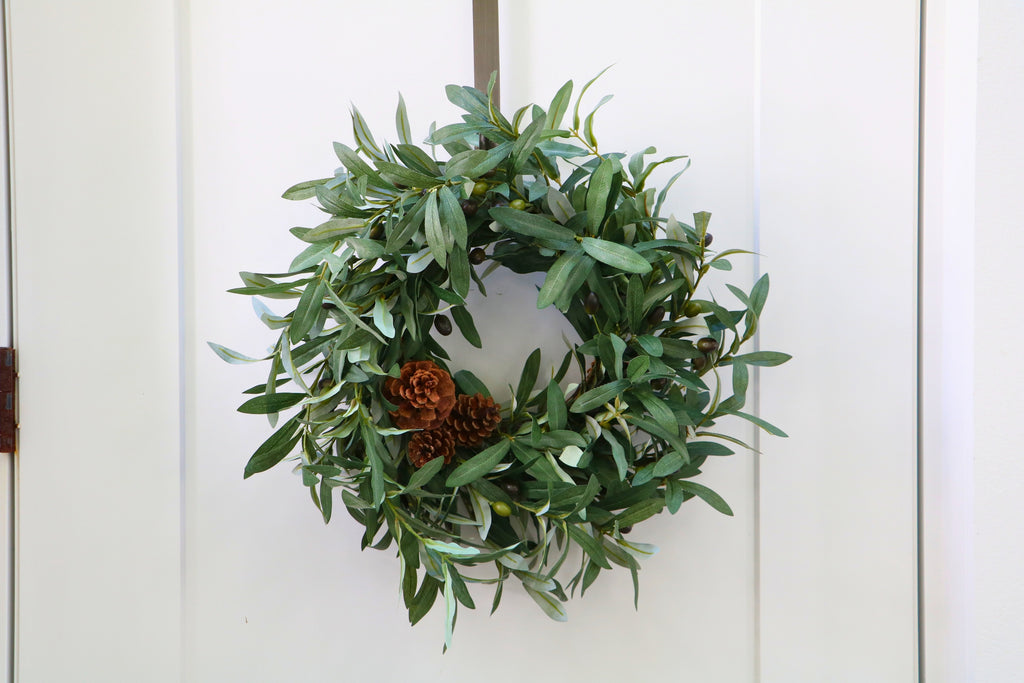 Faux olive wreath with green leaves, decorative olives and a cluster of brown pinecones.