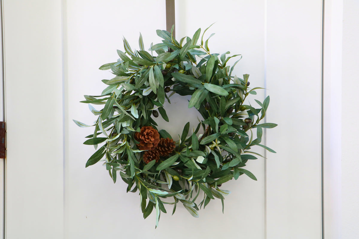 Faux olive wreath with green leaves, decorative olives and a cluster of brown pinecones.